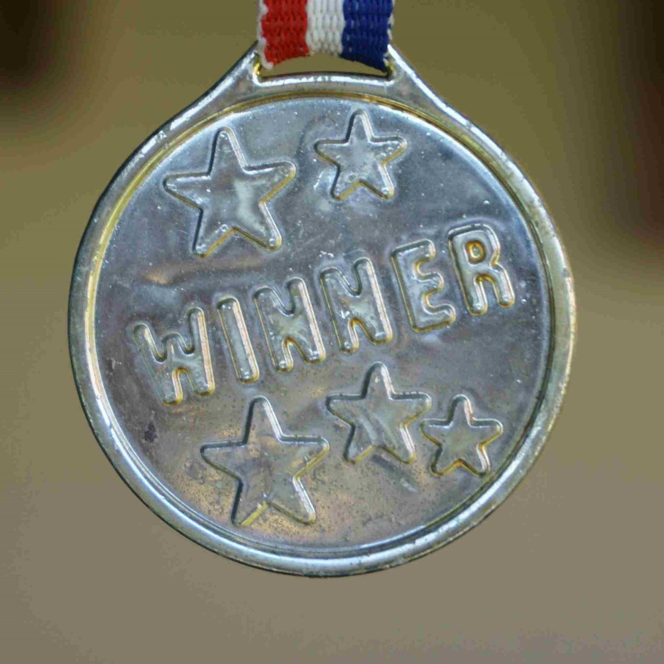 Close up of Medal embossed inscribed "winner" and five starts on the end of a striped lanyard
