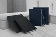 Lifestyle example of two sets of notebooks, navy and black with a navy metal ballpoint pen